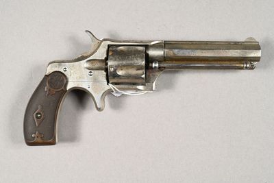 un vieux revolver avec une poignée en bois sur une surface blanche