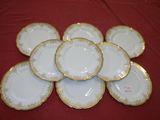 six white and gold plates with gold trim on a red table cloth