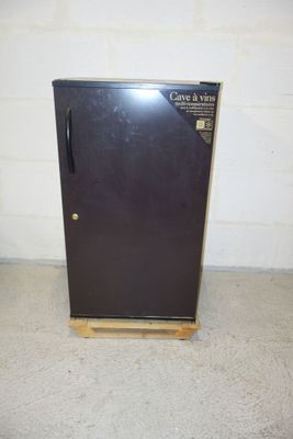 a small black refrigerator in a room with a white brick wall