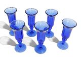 six verres à vin bleus alignés sur une surface blanche