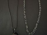 two necklaces with a skull on a chain on a black surface
