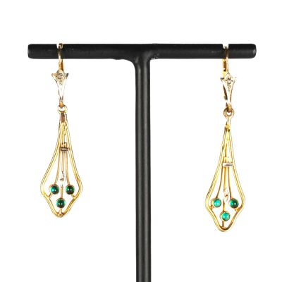 une paire de boucles d'oreilles en or et émeraude posée sur un socle noir