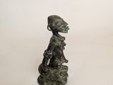 sculpture of a woman sitting on top of a rock on a white surface