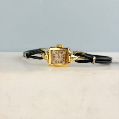 une image représentant une montre dorée et noire posée sur une surface en marbre