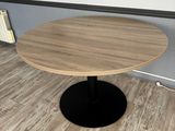a small round table with a black base on a wooden floor