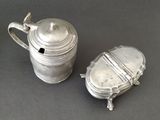 two silverplated teapots with lids and handles on a table