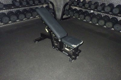 un banc et des haltères dans une salle de sport, avec un support rempli d'haltères
