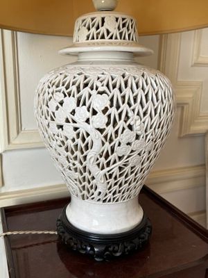 a white vase on a table with a lamp on top of it