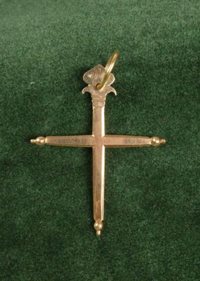 une croix en or ornée d'un oiseau, posée sur un tissu vert