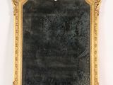 un miroir au cadre doré ouvragé accroché à un mur blanc sur fond noir
