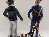 two figurines of men dressed in uniforms and hats stand on wooden bases