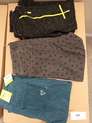 Trois paires de jeans pour homme se trouvent dans une boîte posée par terre.