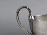 an antique silver cup with a handle on a gray surface