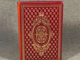 a close up of a red book with gold trim on a gray surface