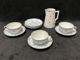 cinq tasses et soucoupes posées sur une table, avec un pichet