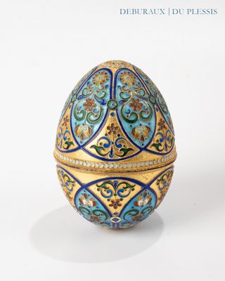 un œuf bleu et doré posé sur une surface blanche