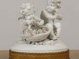 une statue blanche représentant deux chérensils, avec un panier de chérensils posé sur une table
