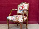 une chaise dont l'assise est recouverte d'un tissu à motifs floraux, placée devant un mur rouge