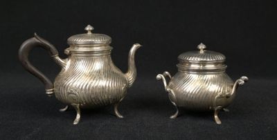 pair of antique silver teapots on stand on black background