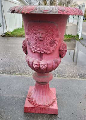 un vase rouge orné d'un visage, posé sur le trottoir