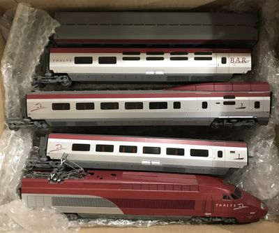 trois trains rouges et argentés se trouvent dans une boîte posée sur une table
