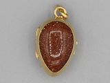 a close up of a gold pendant with a red stone on it