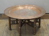 une table sur laquelle est posé un plateau en métal, posée sur un parquet