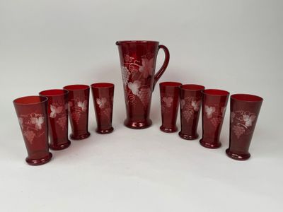six verres rouges et un pichet posés sur une table