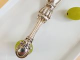 a silver spoon and a green grape on a white plate