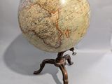 un petit globe terrestre posé sur un trépied, devant un fond blanc