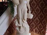 une statue représentant une femme tenant un panier de fleurs, posée sur un socle