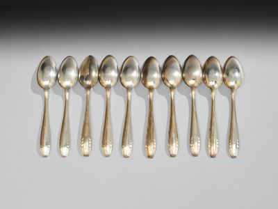 six cuillères en argent sont alignées sur une surface blanche