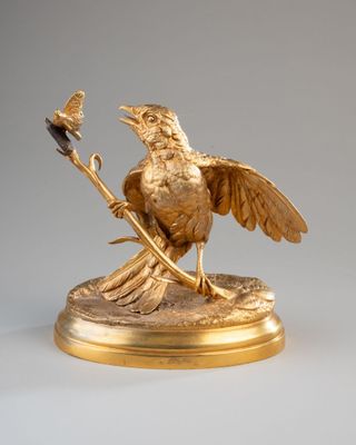une statue en or représentant un oiseau sur une branche, sur laquelle est perché un autre oiseau