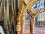a gold framed mirror with a painting on the wall behind it