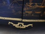 a black and gold painted cabinet with a boat on it
