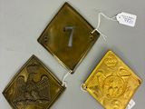 trois plaques et étiquettes en laiton posées sur une table, accompagnées d'étiquettes