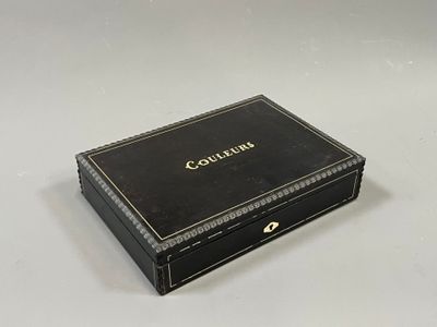 une vieille boîte noire ornée d'une inscription dorée, posée sur une surface blanche