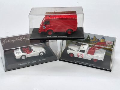 trois petits véhicules jouets dans des boîtes transparentes, posés sur une surface blanche