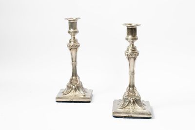 une paire de bougeoirs en argent posés sur des socles, sur fond blanc