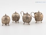 three silver teapots and a sugar bowl on a white surface