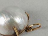 a close up of a white pearl on a gold plated pendant