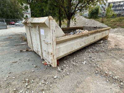 une benne à ordures posée par terre à côté d'un arbre