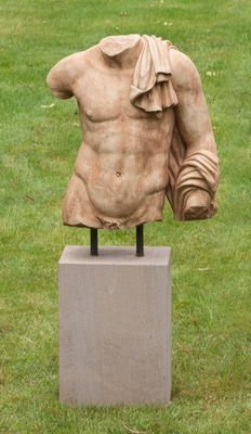 statue représentant un torse masculin posée sur un socle dans un champ herbeux