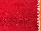 an orange and red rug with a white border on a wooden floor