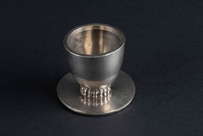 a silver cup on a saucer on a black surface