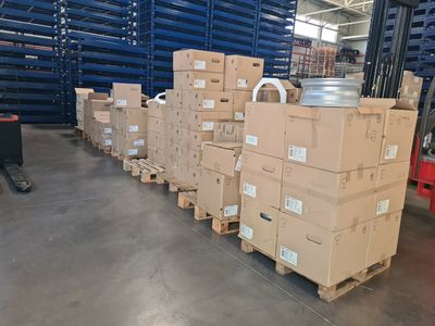 Des cartons sont empilés sur des palettes dans un entrepôt, avec des palettes en arrière-plan.