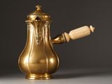 an antique brass coffee pot with a wooden handle on a table
