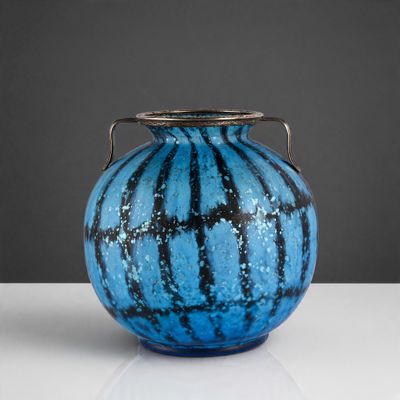 un vase bleu posé sur une table, muni d'une anse en argent