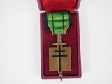 une boîte rouge ornée d'une croix dorée et contenant un ruban vert