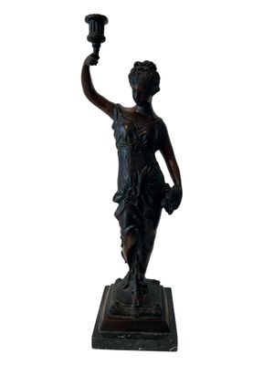 bronze statue of a woman holding a lit candle in her right hand